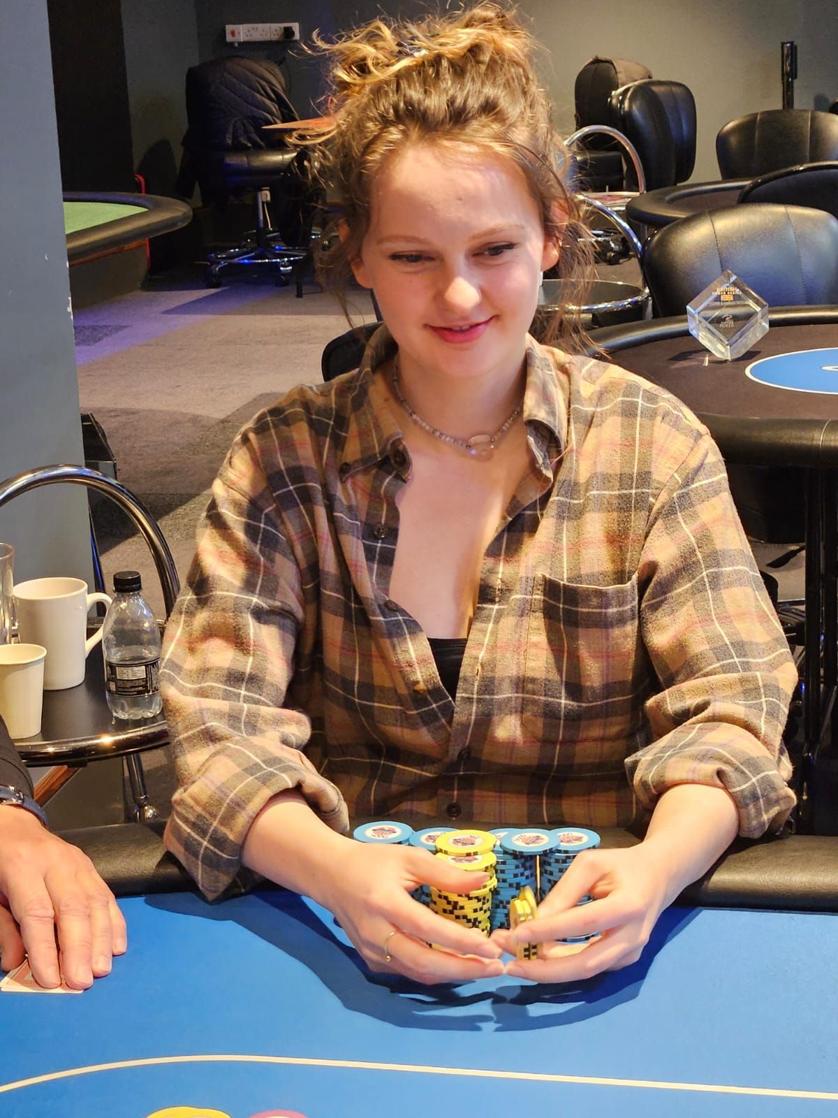 Woman at a poker table with a stack of chips, smiling, wearing a flannel shirt.