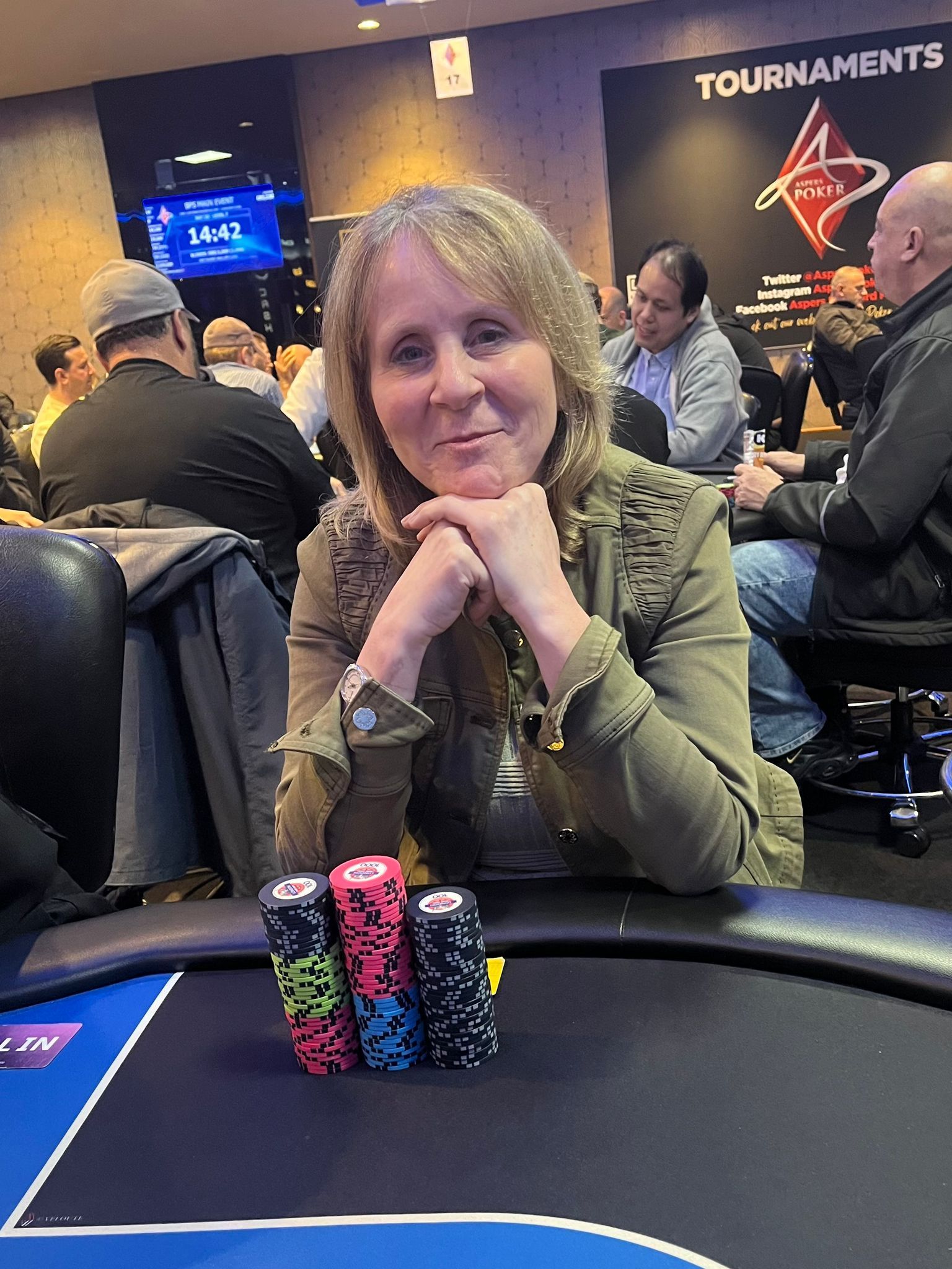 Woman at poker table with chips, smiling. Poker tournament setting.