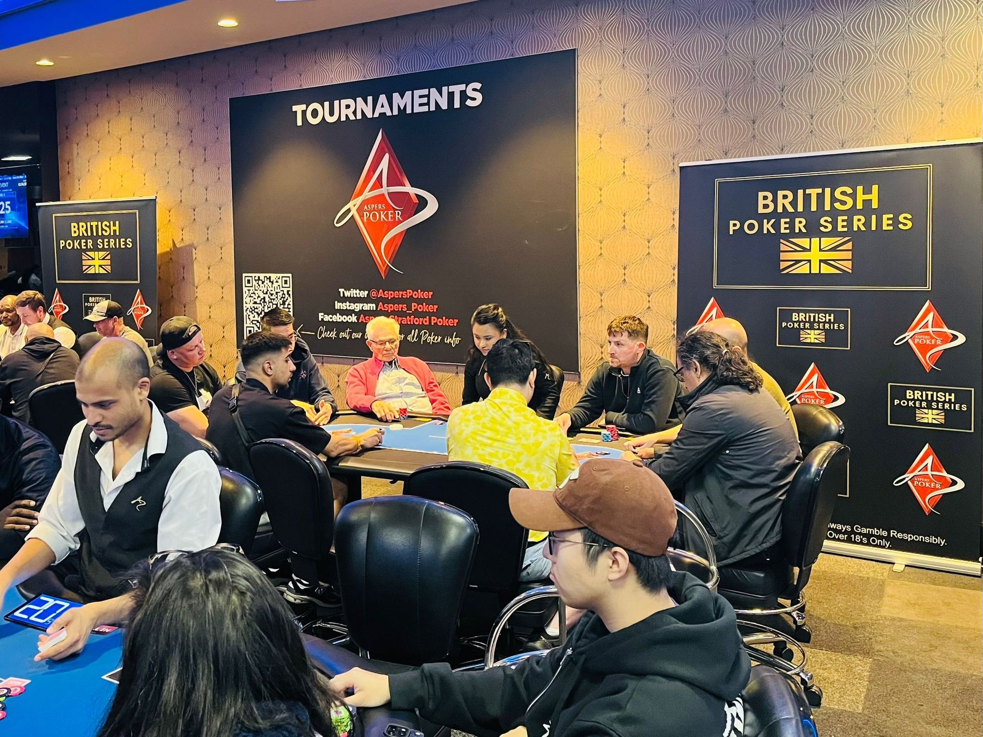 Poker tournament in progress, players seated at a table. 
