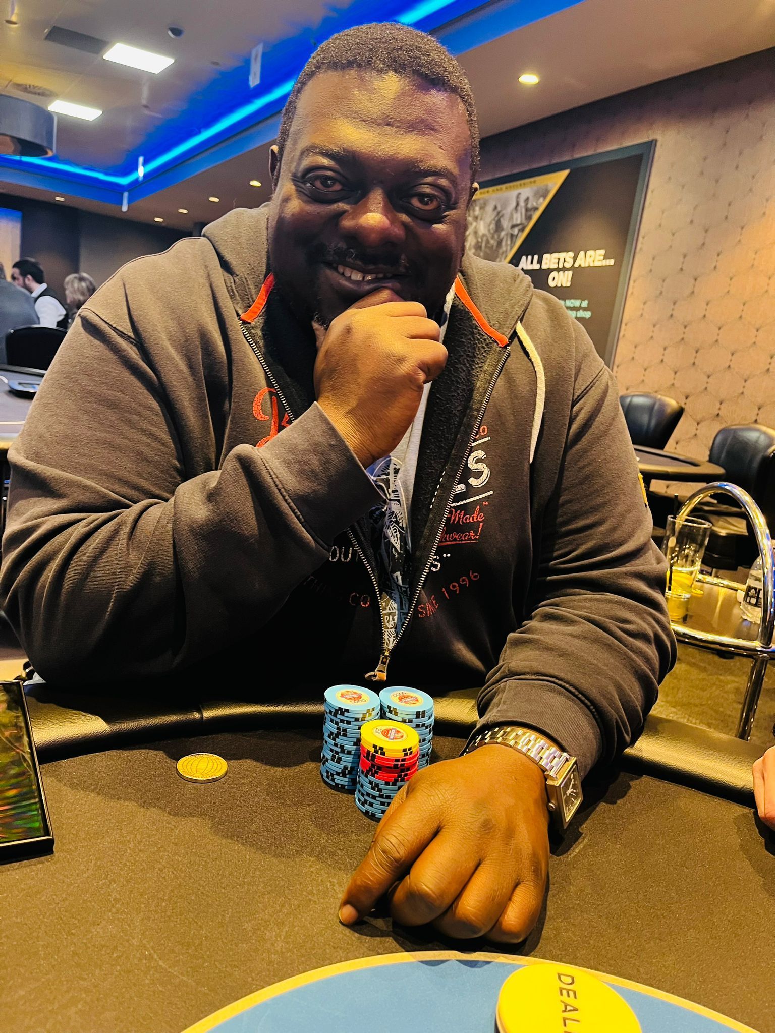 A man with a hand under his chin smiles at a poker table with chips.