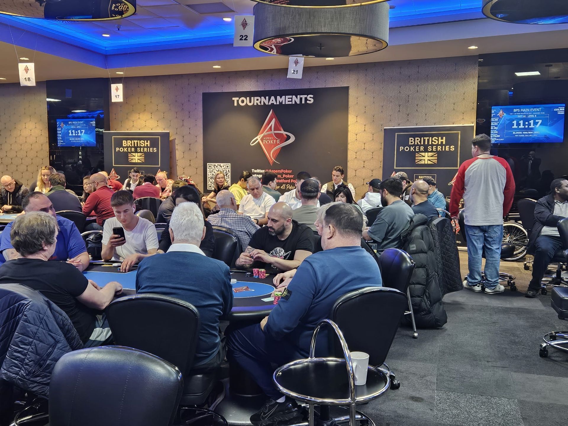 Poker tournament in a brightly lit room with players at tables.