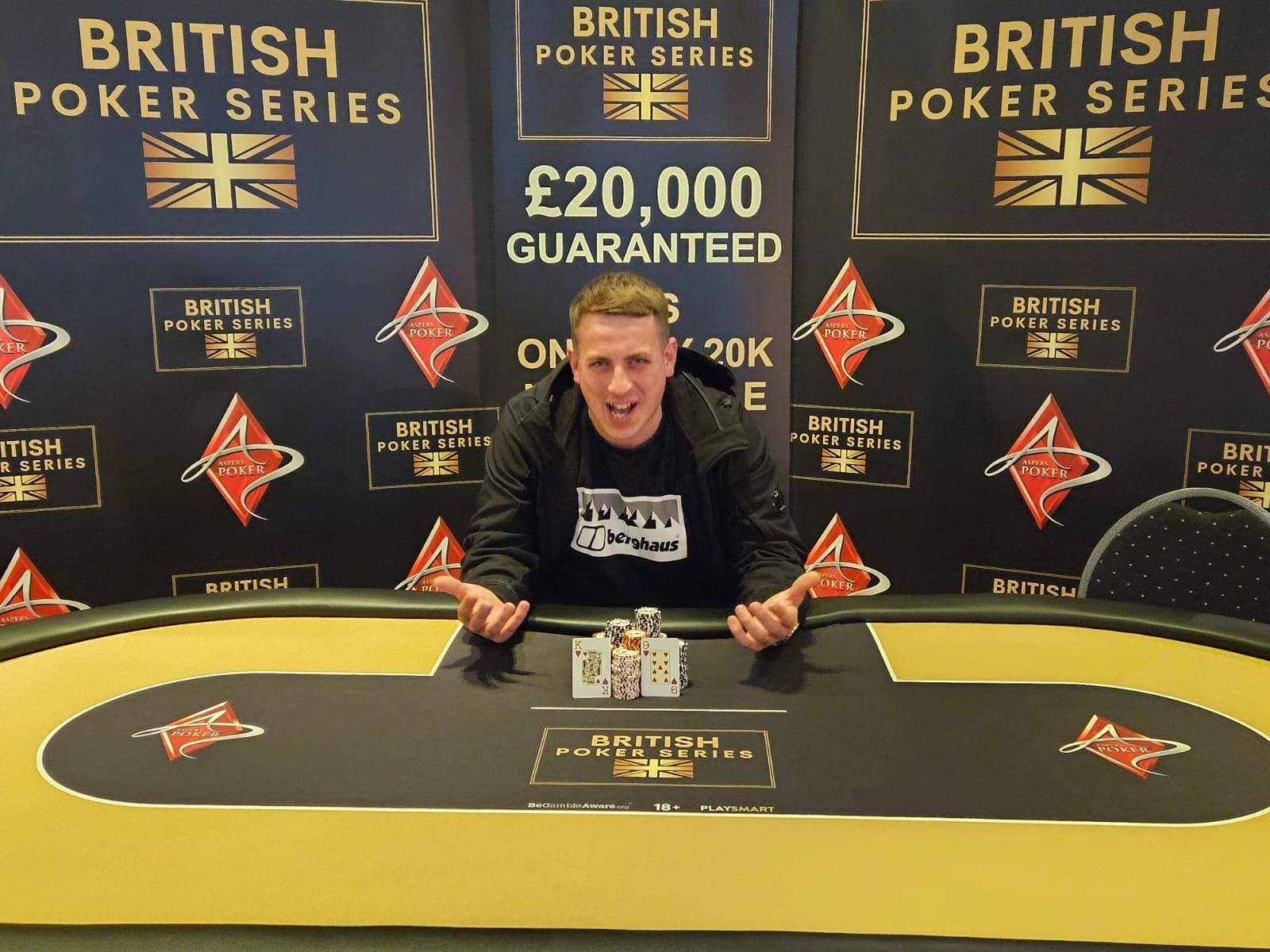 Man celebrating poker win at a British Poker Series table, surrounded by logos and a prize announcement.