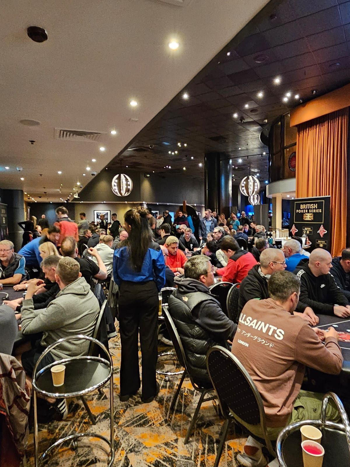 Poker room with many people playing at tables; a waitress stands in the foreground.