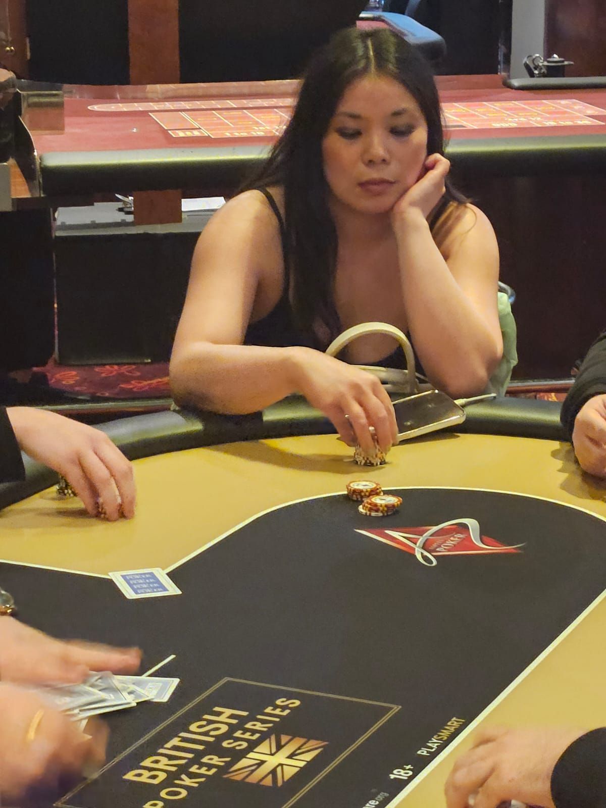 Woman at poker table, resting chin on hand, chips in front of her. Poker table has 