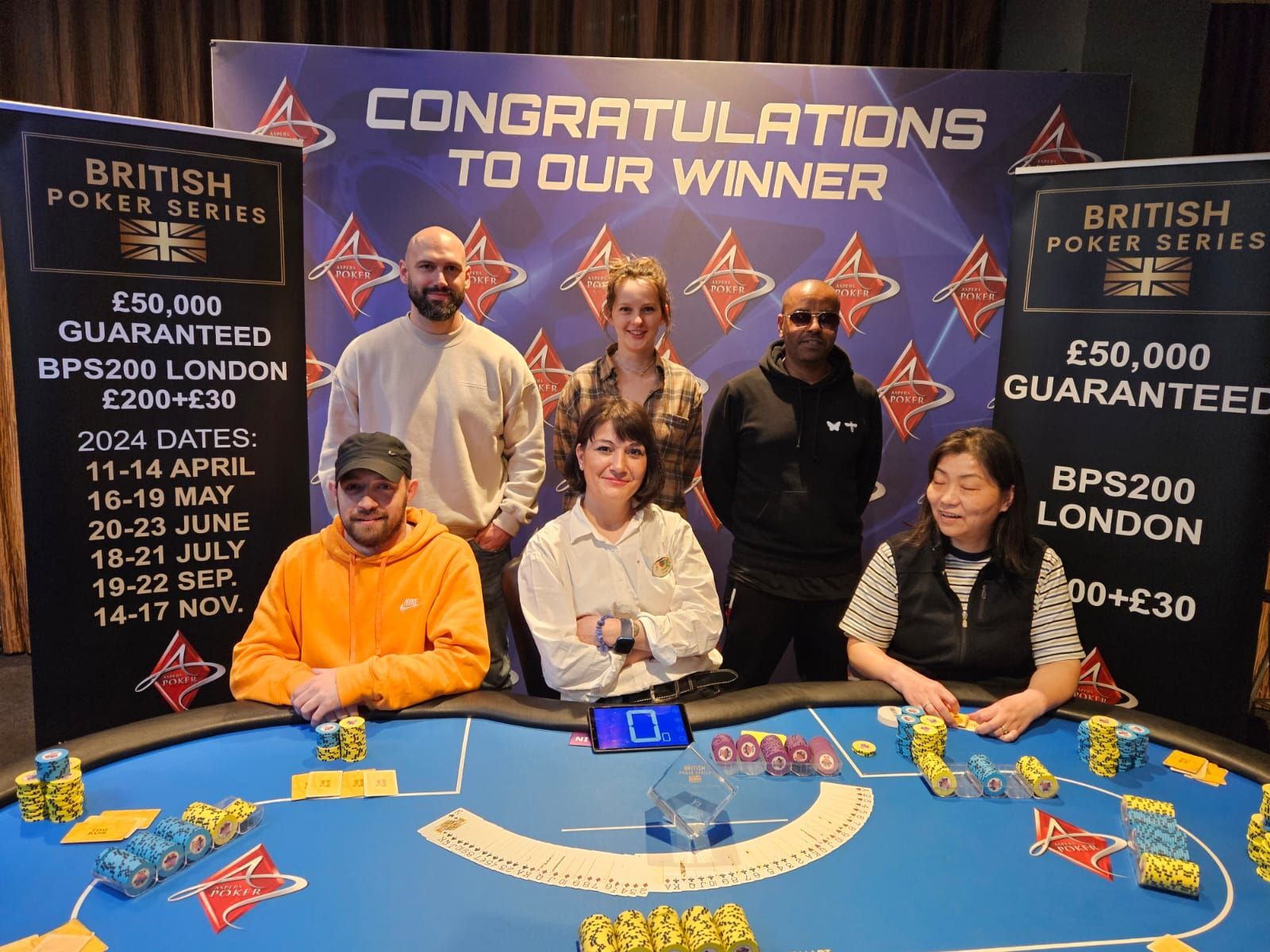 Group of poker players at a table, celebrating a win at a British Poker Series event in London.
