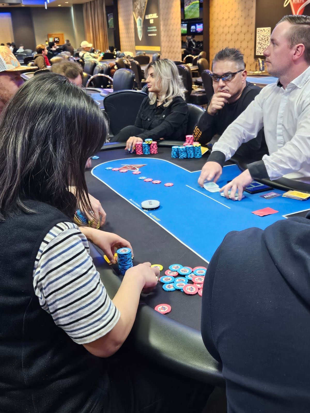People playing poker at a table in a casino; chips and cards are visible; action is in progress.