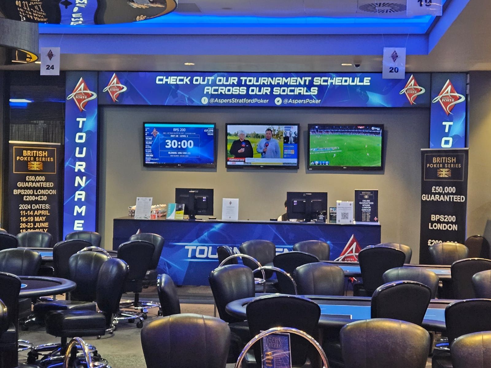 Poker tournament area with tables, chairs, screens showing game info, and schedule banner.