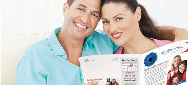 A man and a woman are sitting on a couch holding a newspaper.