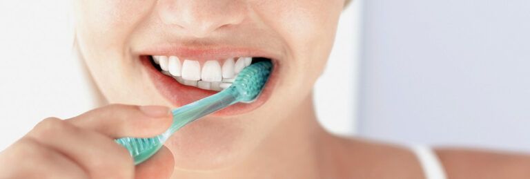 A woman is brushing her teeth with a green toothbrush.