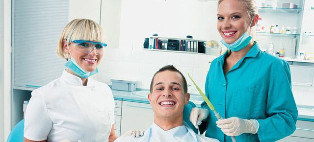 A man is sitting in a dental chair with two dentists standing next to him.