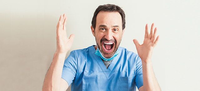 A man in scrubs and a mask is screaming with his hands in the air.