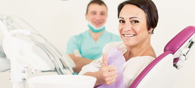 A woman is sitting in a dental chair giving a thumbs up.