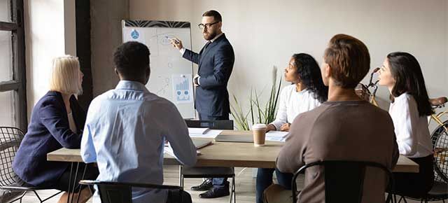 A man is giving a presentation to a group of people sitting around a table.