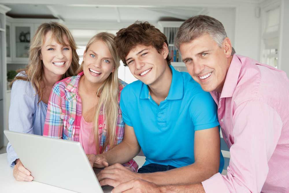 A family is sitting around a table using a laptop computer.