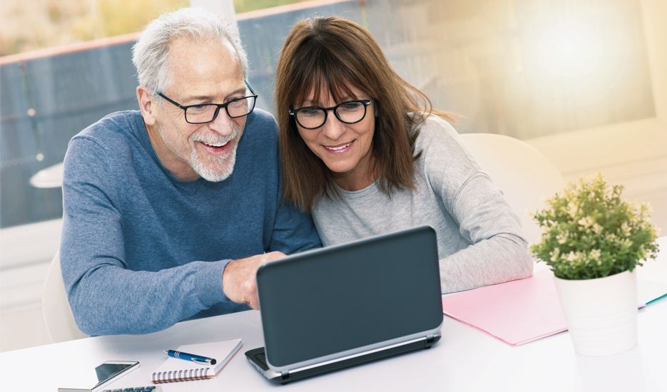 A man and a woman are sitting at a table looking at a laptop computer.