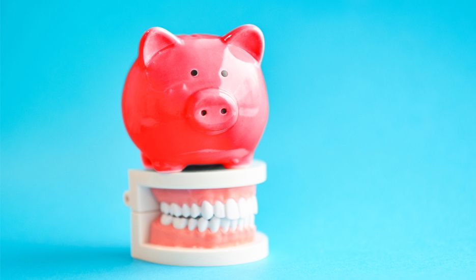 A red piggy bank is sitting on top of a model of teeth.