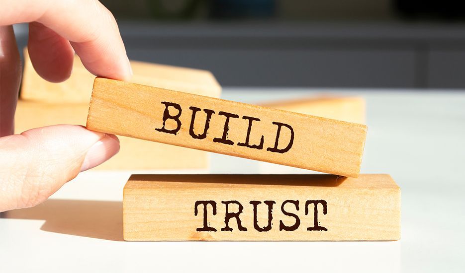A person is holding a wooden block with the words build and trust written on it.