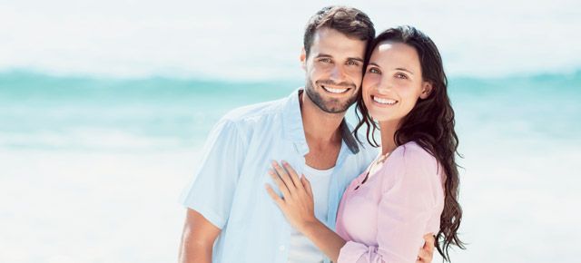 A man and a woman are posing for a picture on the beach.