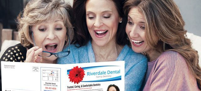 Three women are sitting on a couch reading a magazine.