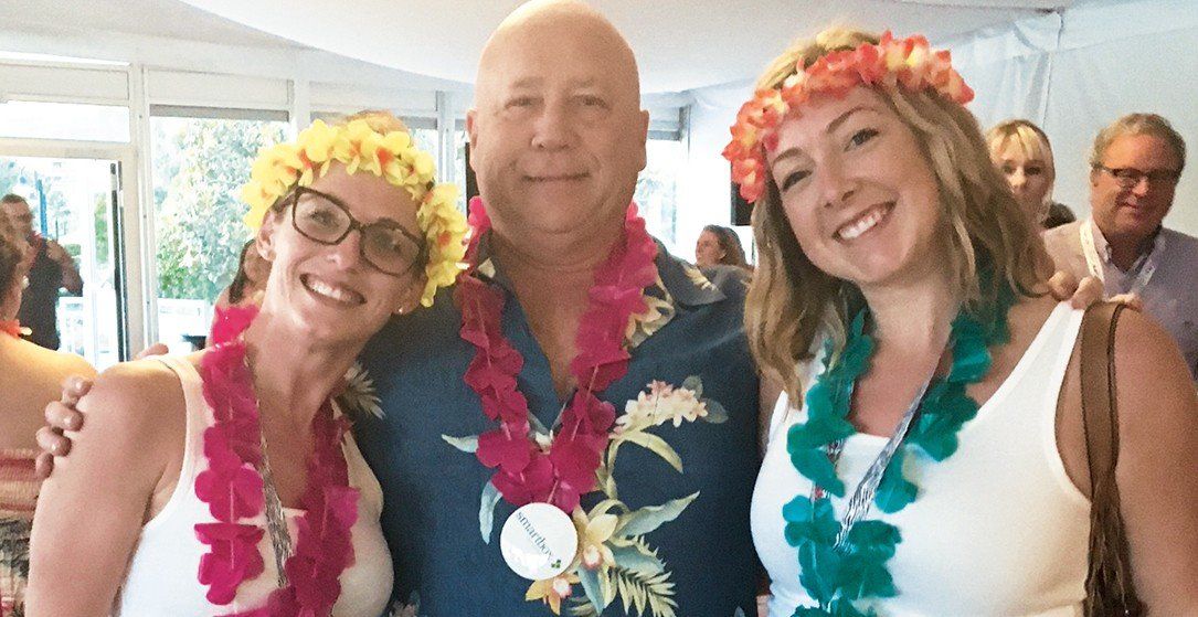 A man and two women wearing lei are posing for a picture.