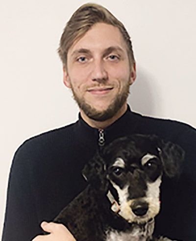 A man is holding a black and white dog in his arms.