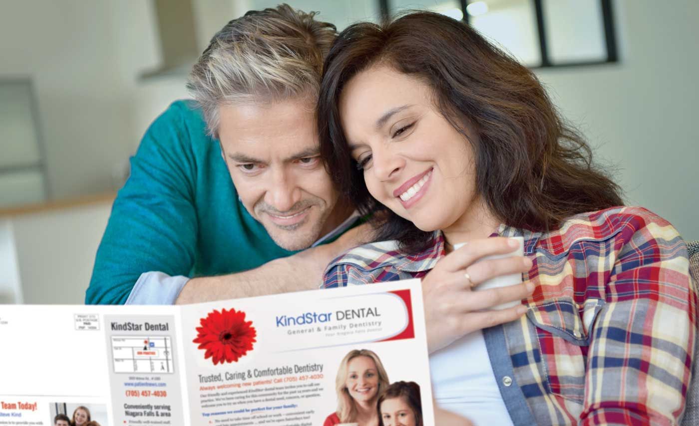 A man and a woman are sitting on a couch looking at a magazine.