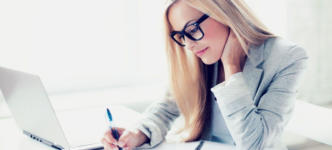 A woman wearing glasses is sitting at a desk in front of a laptop computer.