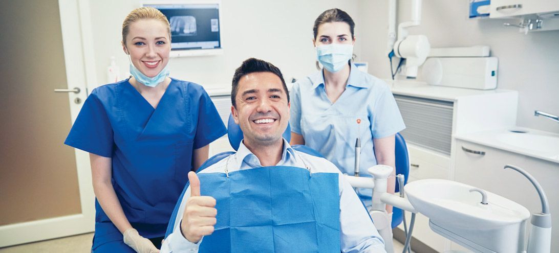 A man is sitting in a dental chair giving a thumbs up.