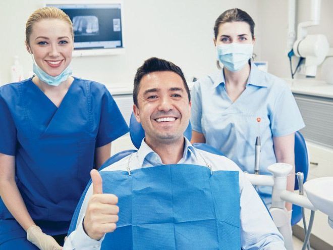 A man is sitting in a dental chair giving a thumbs up.