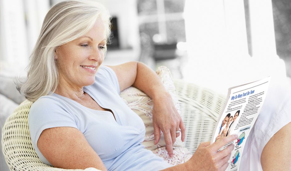 A woman is sitting on a couch reading a magazine.