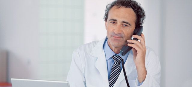 A doctor is talking on a cell phone in front of a laptop.