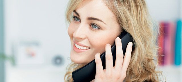 A woman is smiling while talking on a cell phone.