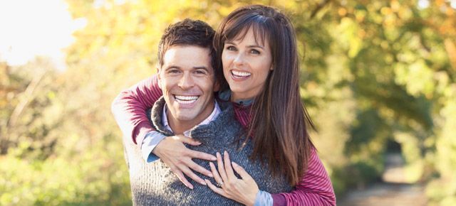 A man is carrying a woman on his back in a park.