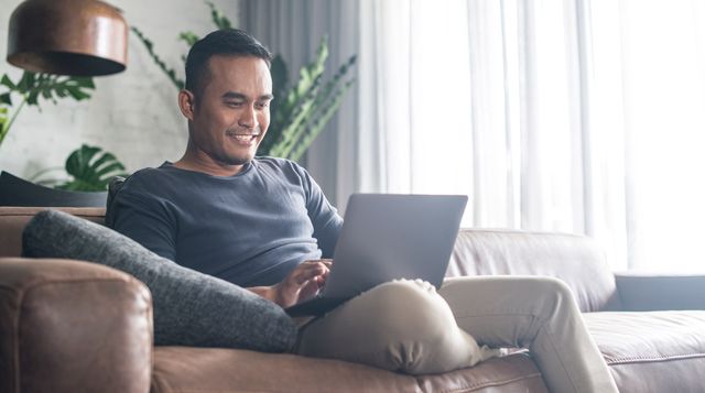 A man is sitting on a couch using a laptop computer.