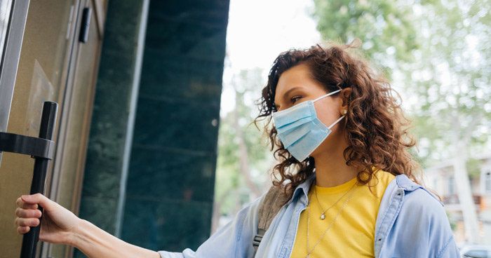 A woman wearing a face mask is opening a door.