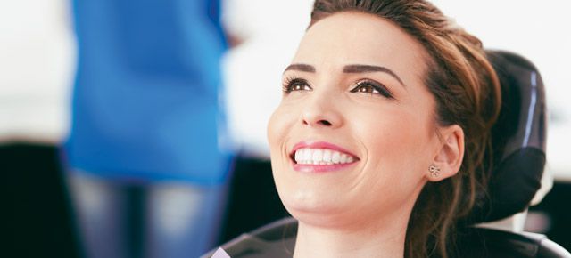 A woman is smiling while sitting in a dental chair.