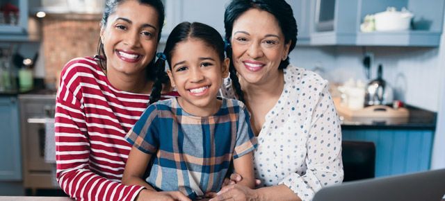 Three women and a little girl are sitting at a table in front of a laptop computer.