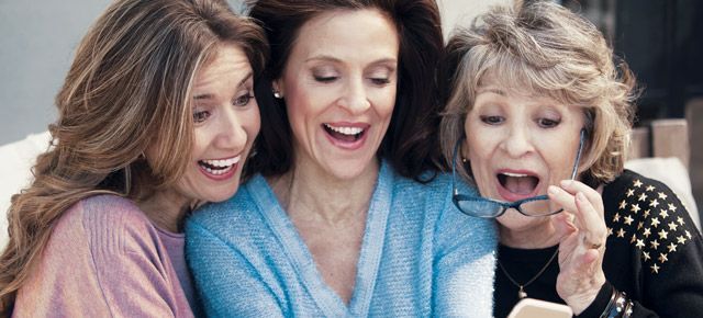 Three women are sitting on a couch looking at a cell phone.