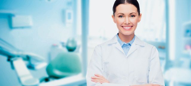 A female dentist is standing in a dental office with her arms crossed.