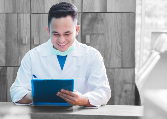 A dentist is sitting at a desk using a tablet computer.