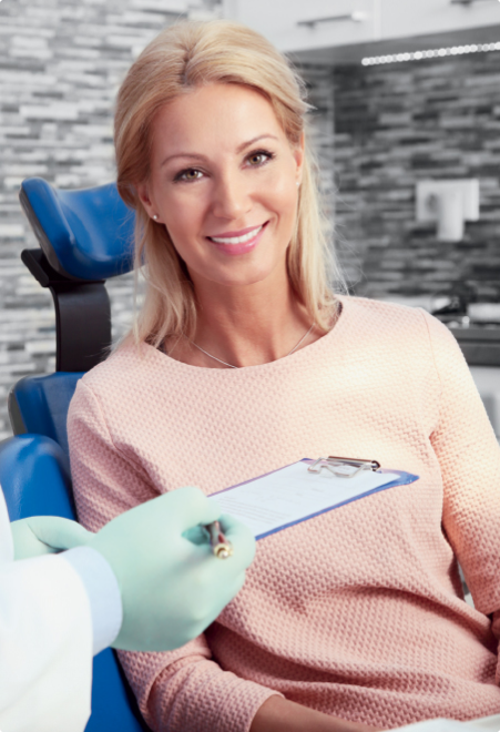 A woman is sitting in a dental chair with a clipboard.