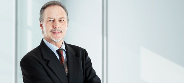 A man in a suit and tie is standing in front of a window with his arms crossed.