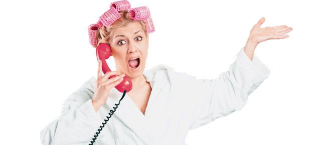 A woman with curlers in her hair is talking on a red telephone.