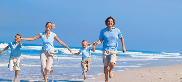 A family is running on the beach holding hands.