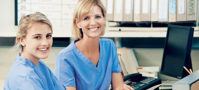 Two nurses are sitting at a desk in front of a computer.