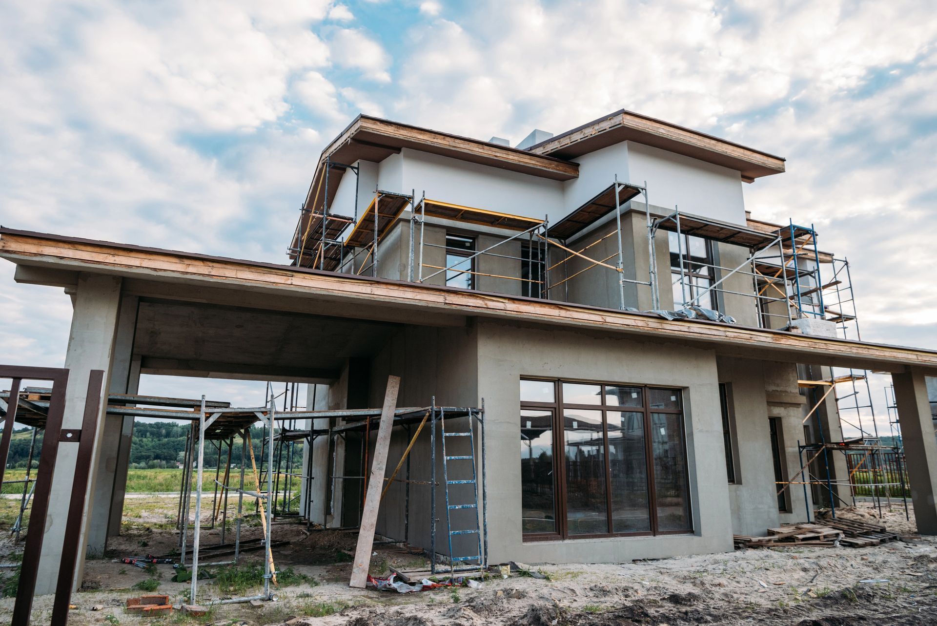Cimentaciones de hormigón para una casa nueva en construcción en un terreno baldío cubierto de tierra, con árboles al fondo.