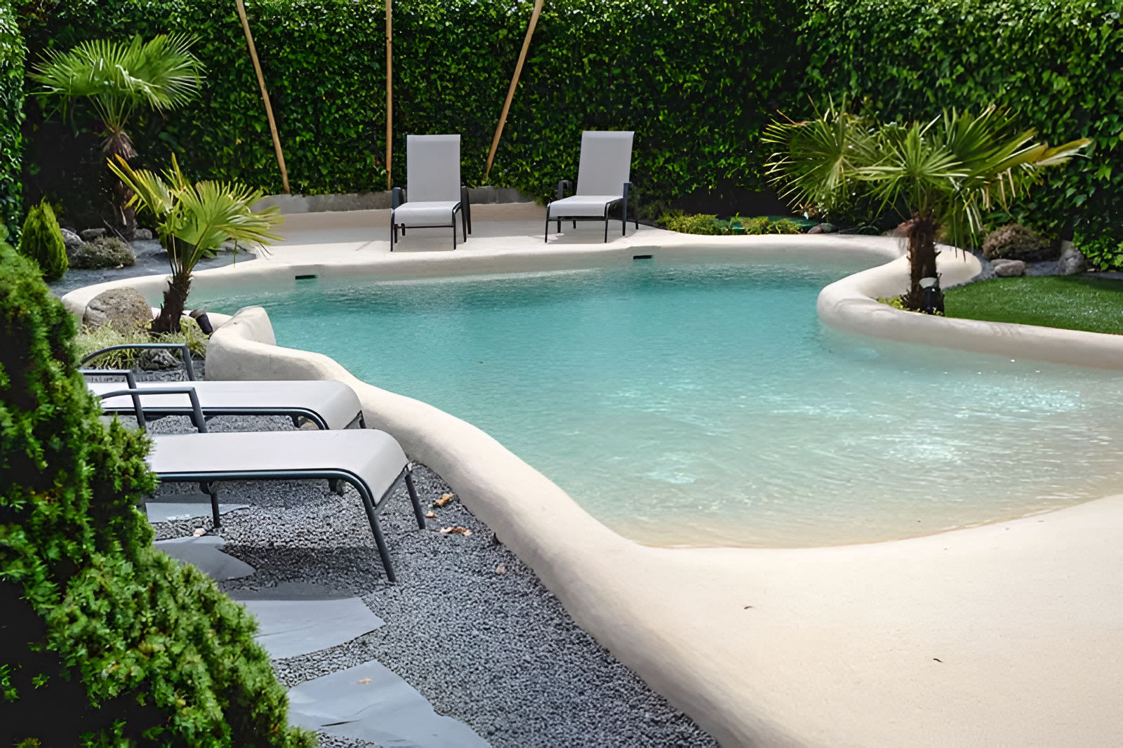 Una piscina de forma curvilínea con entrada tipo playa de color arena, rodeada de grava, tumbonas y palmeras.
