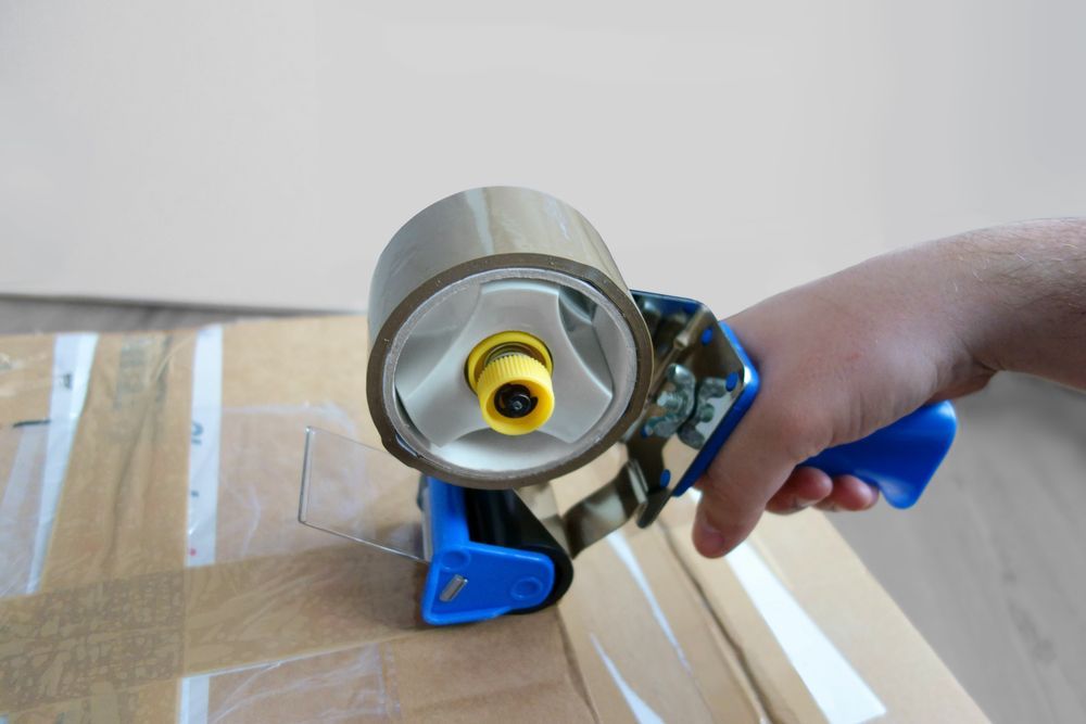 A Person Is Using A Tape Dispenser To Tape A Box — Balzers Removals and Carrying in Plainland, QLD