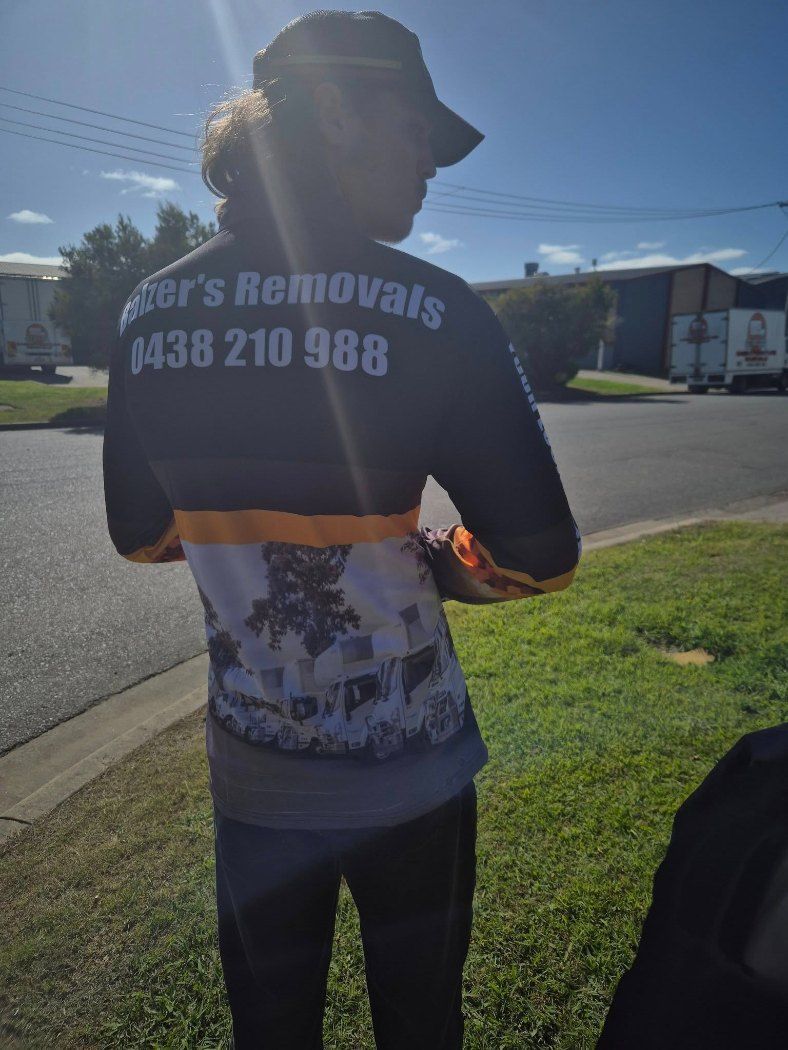 A Man Wearing A Shirt That Says ' Mover 's Removals ' On The Back Is Standing In The Grass — Balzers Removals and Carrying in Helidon, QLD
