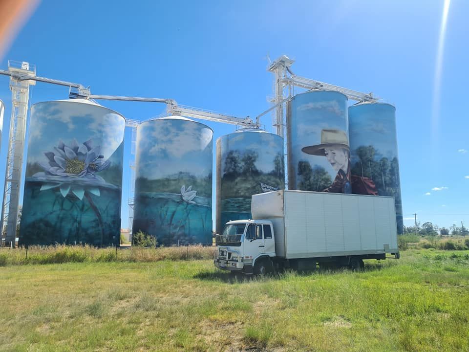 A White Truck Is Parked In Front Of A Row Of Silos With Paintings On Them — Balzers Removals and Carrying in Helidon, QLD